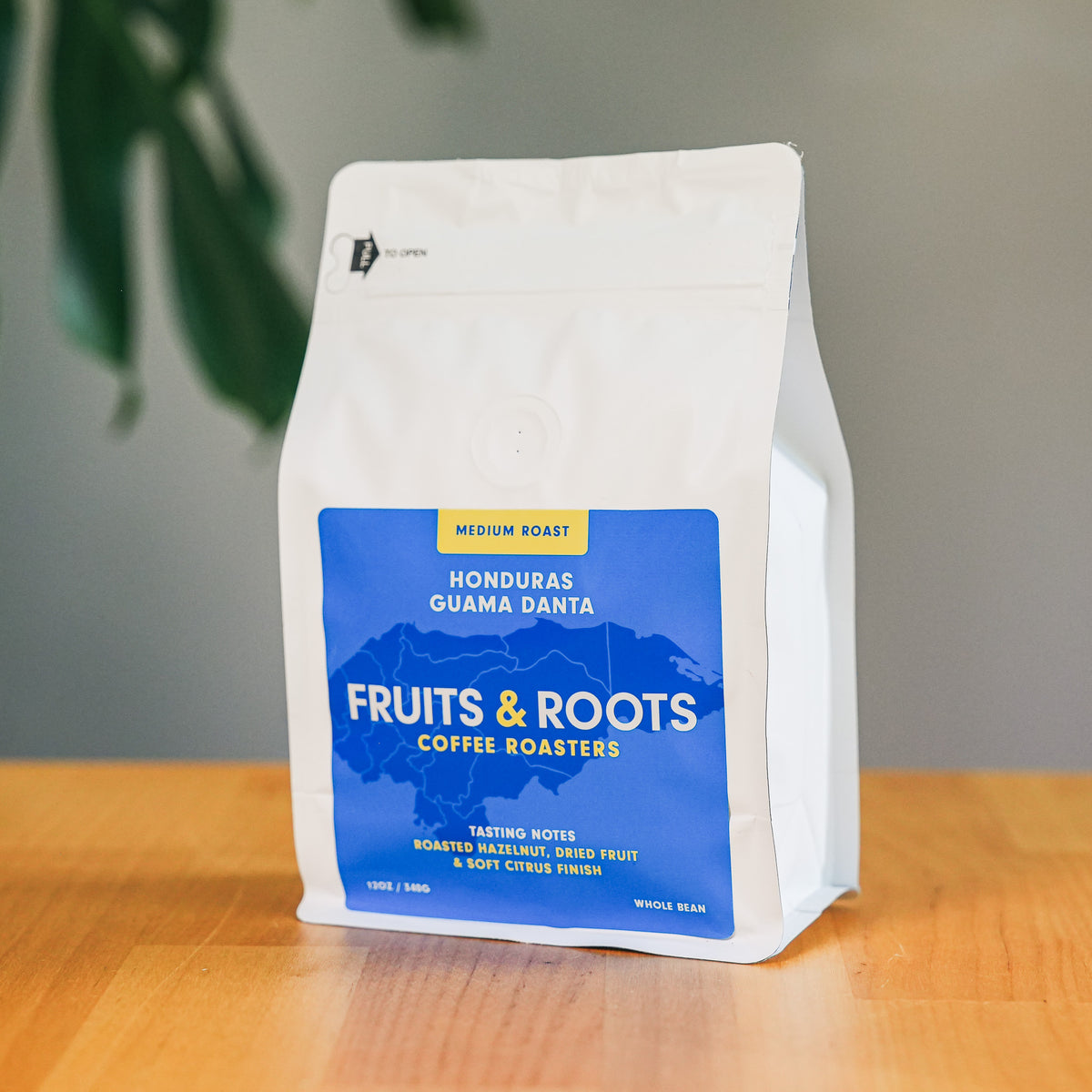 Coffee bag from Fruits & Roots Coffee Roasters on a wooden surface with a plant in the background