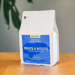 Coffee bag from Fruits & Roots Coffee Roasters on a wooden surface with a plant in the background