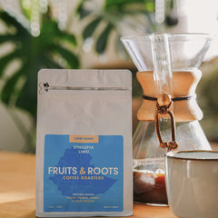 Fruits & Roots coffee package with a Chemex and mug on a wooden surface with plants in the background